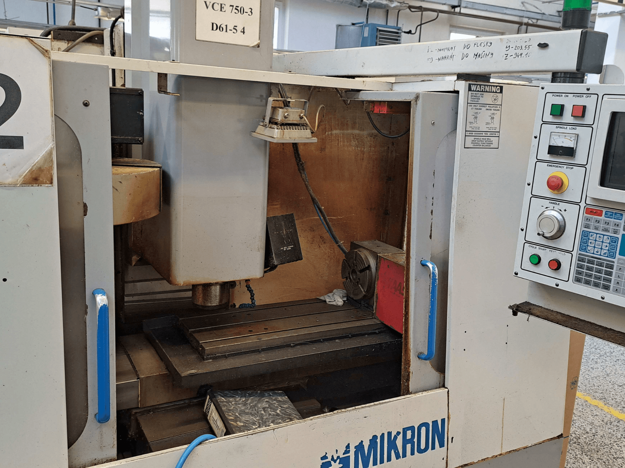 Frontvy av en Mikron VCE 750-3 fräsmaskin, som visar spindel, kontrollpanel och arbetsbord med tekniska detaljer.