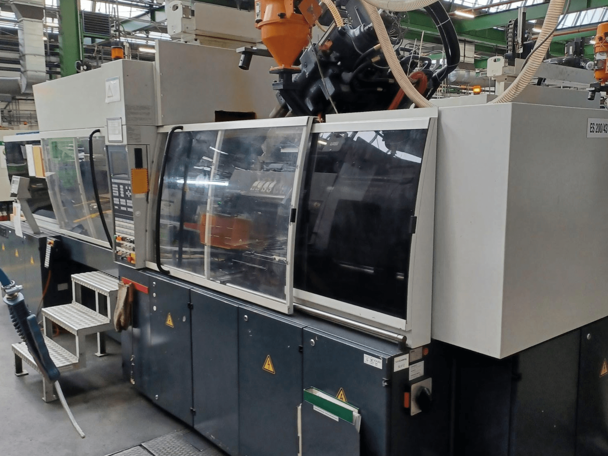 Frontvy av en formsprutningsmaskin för plast, märke och modell okända, med genomskinliga säkerhetsdörrar och kontrollpanel.