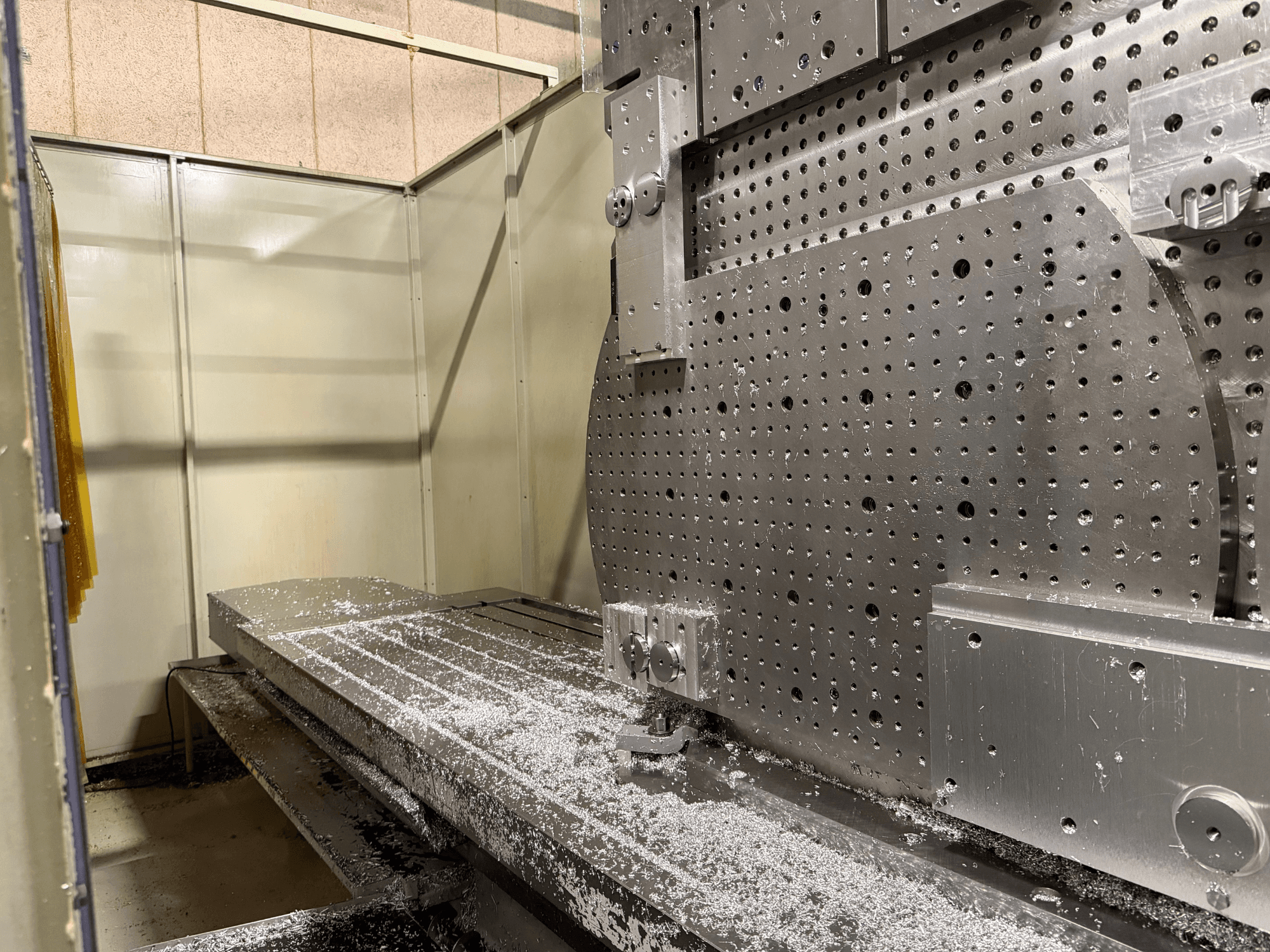 Närbild framifrån av KIHEUNG KNC-U1000 Universal Machining Centre, som visar ett arbetsbord av metall med aluminiumspån.