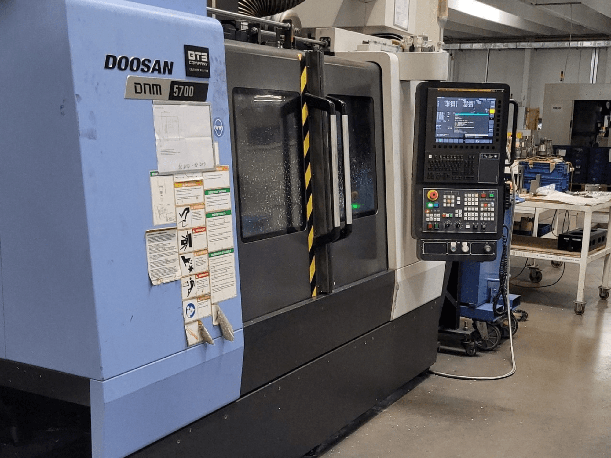 DOOSAN DNM 5700 vertikalt bearbetningscenter, framifrån, med kontrollpanelen och manöverreglagen i förgrunden.
